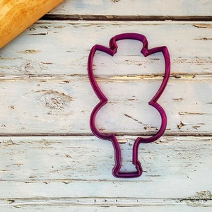 May include: A purple plastic cookie cutter shaped like a tree with a single trunk and a rounded crown.