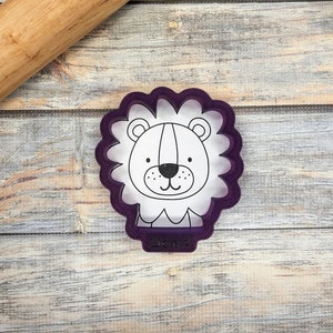 May include: Purple plastic cookie cutter shaped like a lion's head with a white outline. The cutter has the word "Lion" written on the bottom.