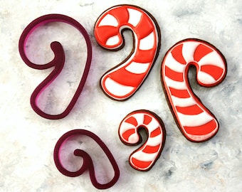 May include: Four candy cane cookie cutters, two red and white candy cane cookie cutters and two purple cookie cutters in the shape of a candy cane.