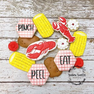 May include: A set of nine decorated sugar cookies with a red, white, and blue gingham pattern. The cookies feature images of corn on the cob, lobsters, and the words "Pinch", "Peel", and "Eat".