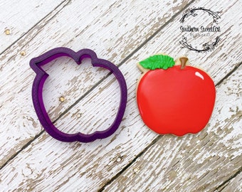 Peut inclure: Emporte-pièce en forme de pomme en plastique violet et un biscuit décoré en forme de pomme rouge et verte.