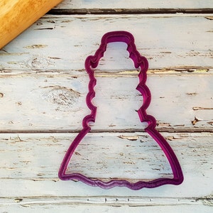 May include: A purple plastic cookie cutter shaped like a dress with a ruffled skirt.