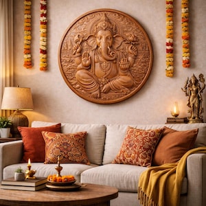 May include: A circular wooden wall plaque featuring a relief carving of the deity Ganesha, depicted with four arms, a trunk, and ornate jewelry. The carving is mounted on a wall above a sofa with orange and patterned throw pillows and a yellow blanket.
