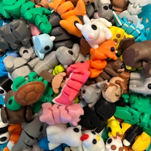 Puede incluir: Una colección de figuras de animales coloridas de varias formas y tamaños. Las figuras incluyen un conejo blanco, un pez naranja, un koala gris y una tortuga verde. Las figuras son de plástico y están en una cesta azul.