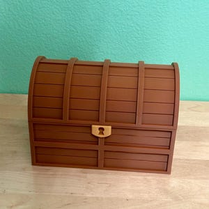 May include: A brown treasure chest with a curved top and a keyhole. The chest is made of wooden planks and has a rectangular shape. The chest is a decorative item.