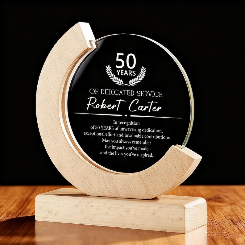 May include: A clear glass award with a wooden base and frame. The award features the text "50 YEARS OF DEDICATED SERVICE" and the name "Robert Carter". The text is in white against a black background.