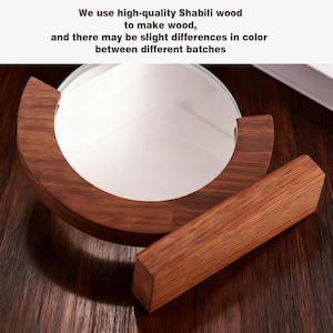 May include: A round, white mirror set in a dark brown, semi-circular wooden frame, with a matching rectangular wooden stand. The text in the image reads: "We use high-quality Shabili wood to make wood, and there may be slight differences in color between different batches."