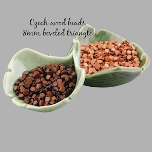 May include: Two bowls filled with 8mm beveled triangle wood beads. One bowl contains brown beads and the other contains orange beads. Czech wood beads.