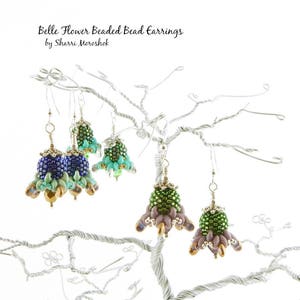 Könnte beinhalten: Vier Paar Perlenblumenohrringe in verschiedenen Farben, darunter Grün, Blau und Lila. Die Ohrringe hängen an einem drahtförmigen, baumförmigen Ohrringständer. Die Ohrringe heißen "Belle Flower Beaded Bead Earrings" von "Sharrie Moroshok".