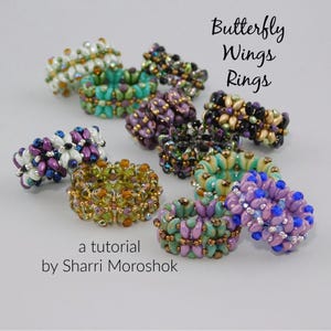 May include: A collection of beaded rings in various colors, including green, purple, gold, and blue. The rings are arranged on a light gray surface. Text on the image reads "Butterfly Wings Rings" and "a tutorial by Sharri Moroshok."