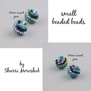 May include: Two pairs of small beaded beads, one pair is 12mm round and the other is 10mm round. The beads are multi-colored with shades of green, blue, black, and silver. The beads are arranged on a gray surface. The text "small beaded beads" is written in black cursive above the beads. The text "by Sharri Moroshok" is written in black cursive below the beads.