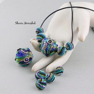 May include: A necklace with a large, multi-colored beaded pendant and smaller matching beads. The beads are made of glass and have a swirling pattern of blue, green, and silver.
