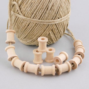 May include: A natural twine ball with a strand of wooden spools strung together. Several loose wooden spools are also visible. The spools are light-colored and cylindrical, with a hole through the center. The twine and spools are likely for crafting or decorative purposes.