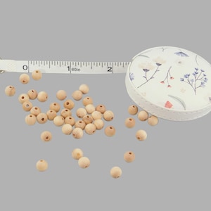 May include: A white tape measure with a floral pattern on the case, and a scattering of natural wood beads.