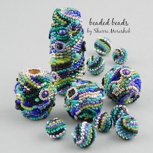 May include: A collection of beaded beads in shades of blue, green, black, and silver. The beads are arranged in a circular pattern on a light gray surface. The beads are all different sizes and shapes, and they are all made of small beads that are sewn together. The beads are all very intricate and detailed.