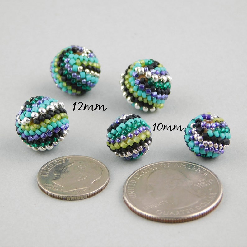May include: Four colorful beaded spheres in shades of green, blue, black, and silver. The beads are 10mm and 12mm in diameter. The beads are shown next to a US quarter for size comparison.