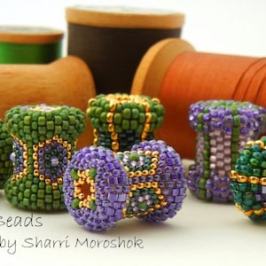 May include: Close-up of six colorful beaded bobbins, each with a different pattern of green, purple, and gold beads. The bobbins are arranged on a white surface, with spools of thread in the background. The text "Bobbin Beads a tutorial by Sharri Moroshok" is visible at the bottom of the image.