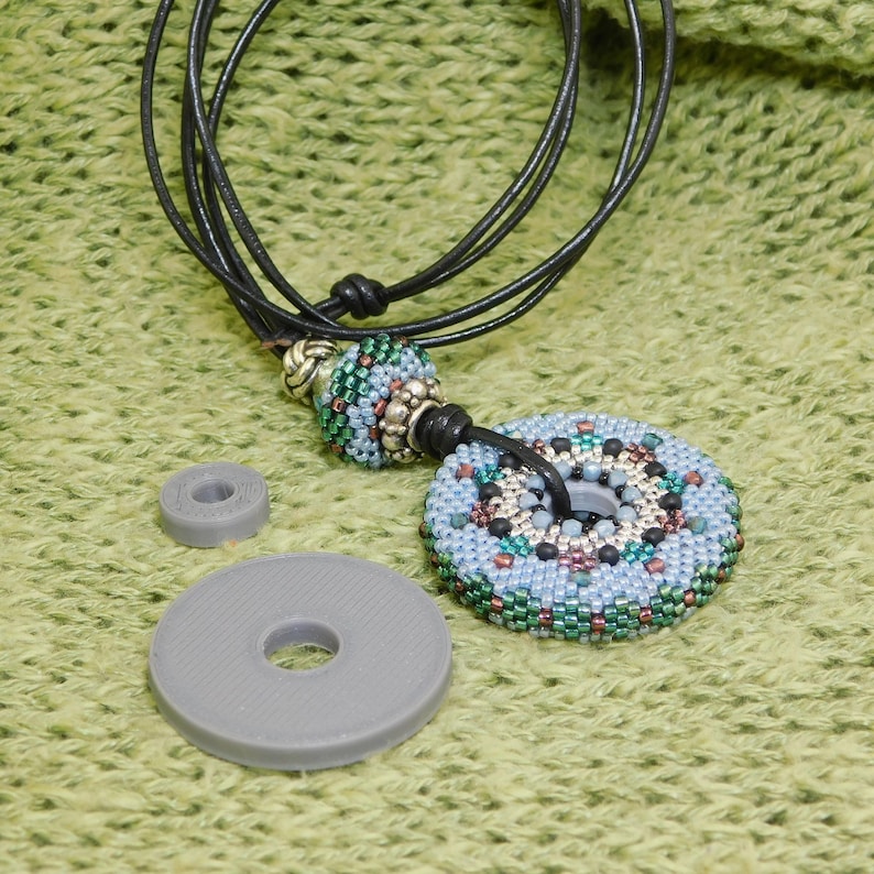 1 Large and 1 small silver gray 3D printed resin disc pictured beside a finished beadwork necklace in which the discs are used as base armatures.