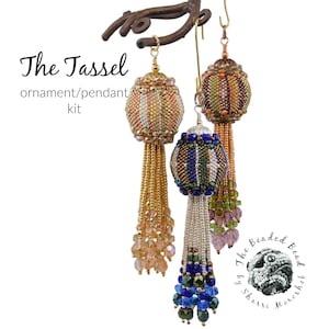 Puede incluir: Tres adornos de borla de cuentas, cada uno con un esquema de color diferente. Los adornos cuelgan de una rama de metal. El texto "The Tassel ornament/pendant kit" es visible en la parte superior de la imagen. El texto "The Beaded Bead by Sharri Monroe" es visible en la parte inferior de la imagen.