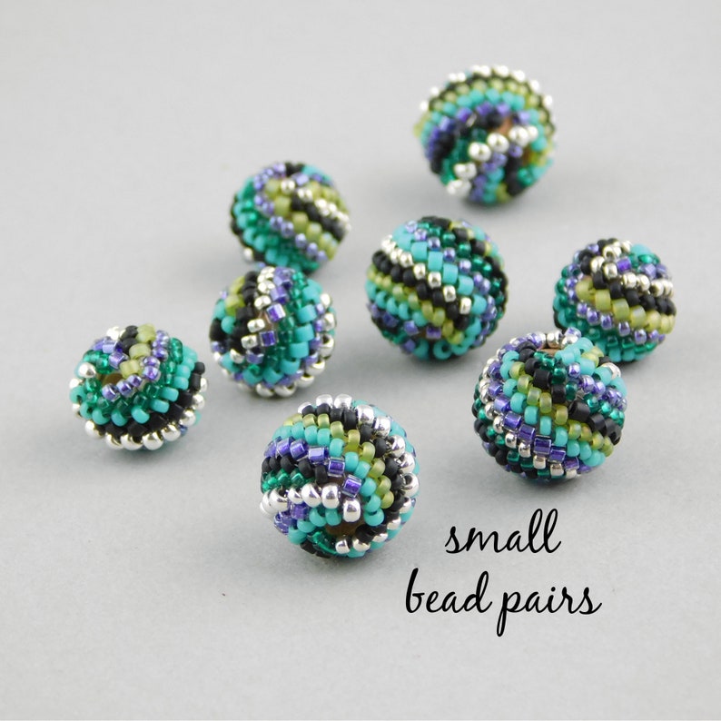 May include: Close-up of eight small, colorful, beaded spheres. The beads are made of black, green, blue, and silver beads. The beads are arranged in a random pattern. The text "small bead pairs" is written below the beads.