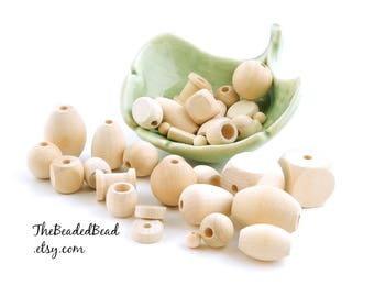 May include: A collection of natural wood beads in various shapes and sizes, including round, oval, and square beads. The beads are displayed in a green ceramic bowl and on a white surface. The text "TheBeadedBead.etsy.com" is visible in the lower left corner of the image.