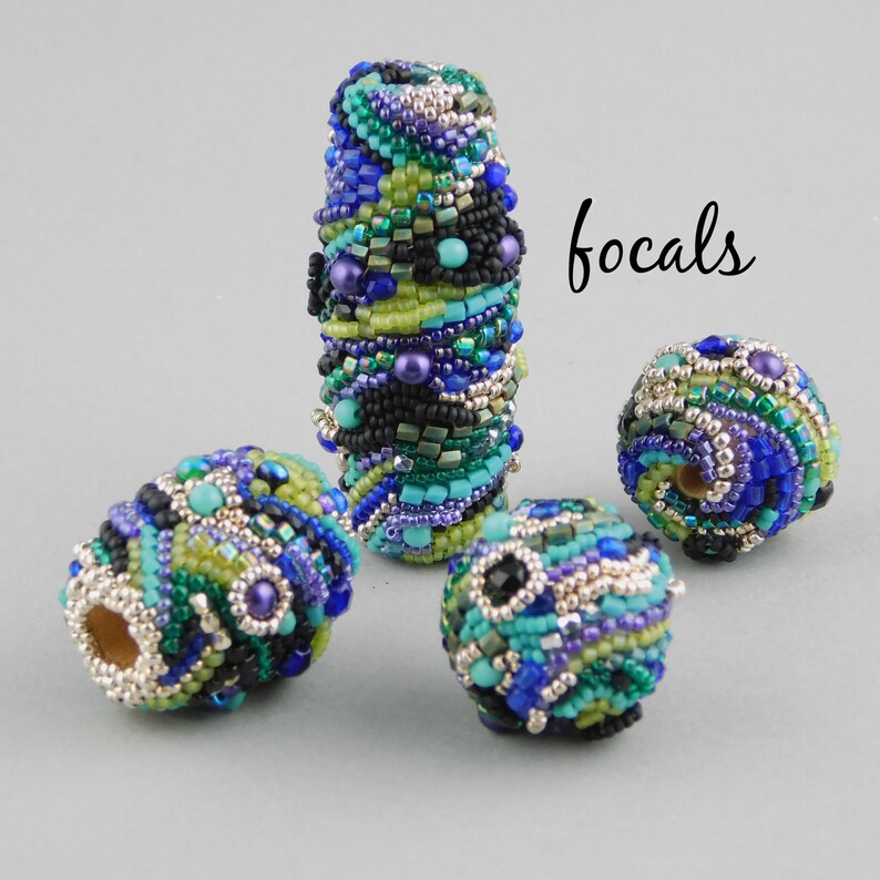May include: Four colorful beaded focal beads in shades of blue, green, black, and silver. The beads are round and oval shaped and have a variety of textures. The word "focals" is written in black ink on a white background.
