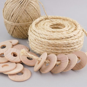 May include: A collection of natural craft supplies. Includes a large coil of thick rope, a ball of twine, and several wooden rings with holes in the center. The rope and twine are beige, and the wooden rings are light brown.