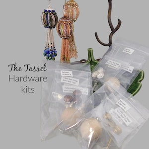 May include: Assortment of tassel hardware kits in clear plastic bags. The kits include wooden beads, metal caps, and other embellishments. The text on the bags reads "The Tassel Hardware Kit" and "11.5mm Nuno Design Acorn Bead Caps".