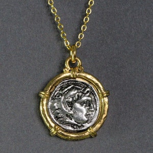 May include: A gold-toned chain necklace with a circular pendant. The pendant features a silver-colored coin with a profile of a person's face. The coin is set in a gold-colored frame.