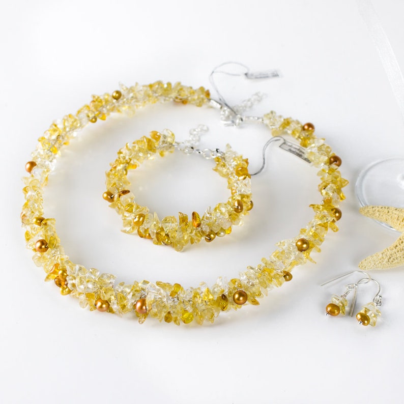 K&ouml;nnte beinhalten: Ein Schmuckset aus gelbem Citrin mit einer Halskette, einem Armband und Ohrringen. Die Halskette und das Armband bestehen aus kleinen, unregelm&auml;&szlig;igen Citrin-St&uuml;cken und kleinen goldenen Perlen. Die Ohrringe sind einfache Silberhaken mit einem einzelnen Citrin-Stein und einer goldenen Perle.
