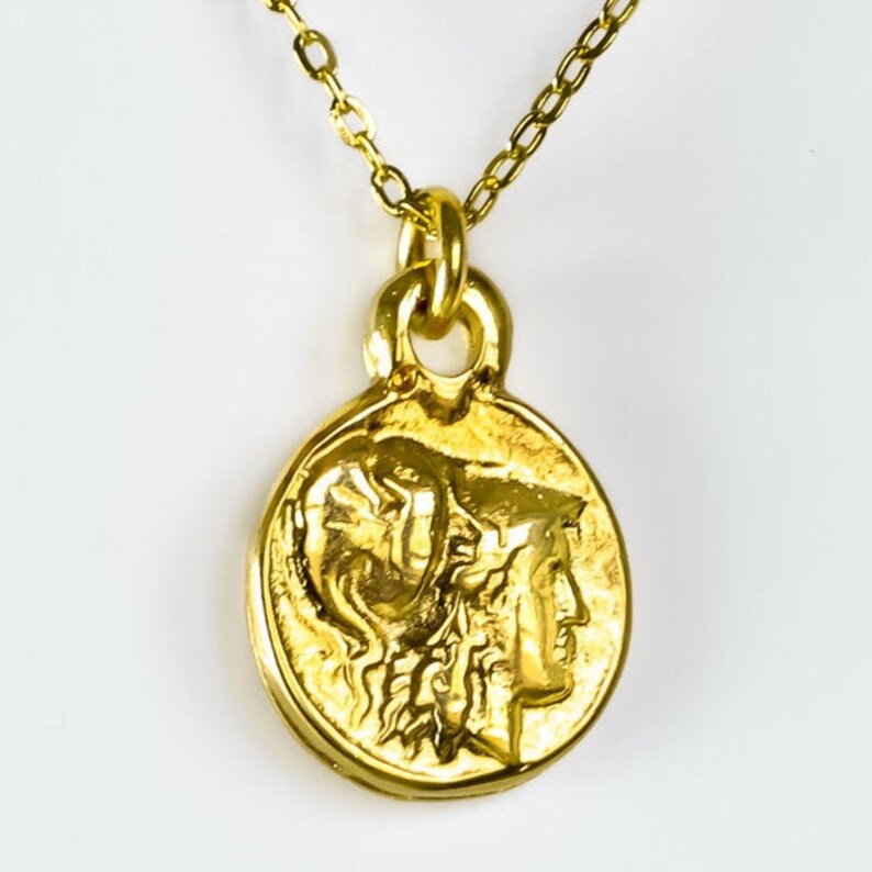Peut inclure: Un collier en cha&icirc;ne dor&eacute;e avec un pendentif rond repr&eacute;sentant un profil d&eacute;taill&eacute; d'un visage de femme. Le pendentif est une r&eacute;plique d'une ancienne pi&egrave;ce de monnaie grecque.