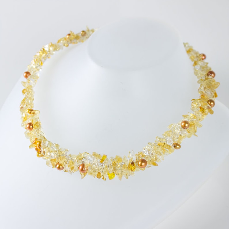 K&ouml;nnte beinhalten: Eine goldene und klare Kristallkette mit kleinen goldenen Perlen. Die Kette besteht aus kleinen, unregelm&auml;&szlig;igen Kristallst&uuml;cken und ist auf einem Draht aufgef&auml;delt.