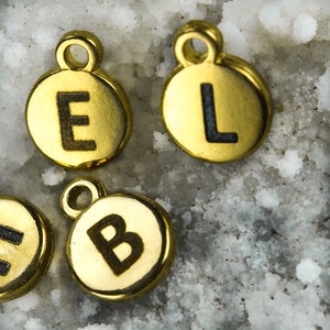 Peut inclure: Quatre breloques en m&eacute;tal de couleur dor&eacute;e de forme ronde avec une lettre noire imprim&eacute;e sur chacune. Les lettres sont E, L, B et une quatri&egrave;me lettre partiellement masqu&eacute;e.