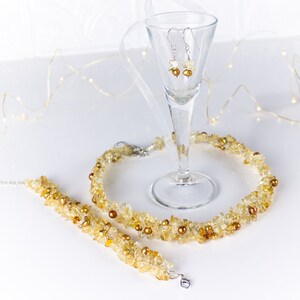 K&ouml;nnte beinhalten: Ein Schmuckset aus Citrin-Edelsteinen mit einer Halskette, einem Armband und Ohrringen. Die Halskette und das Armband bestehen aus kleinen, unregelm&auml;&szlig;igen Citrin-St&uuml;cken und kleinen goldenen Perlen. Die Ohrringe sind silberfarben mit kleinen Citrin-Steinen.