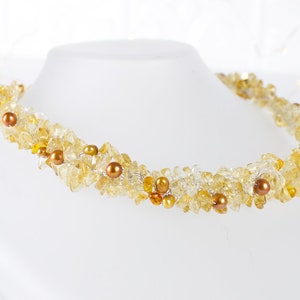 K&ouml;nnte beinhalten: Eine Halskette aus goldenen und gelben Edelsteinen mit kleinen braunen Perlen. Die Kette ist aus Draht gefertigt und zu einer Spirale gedreht.