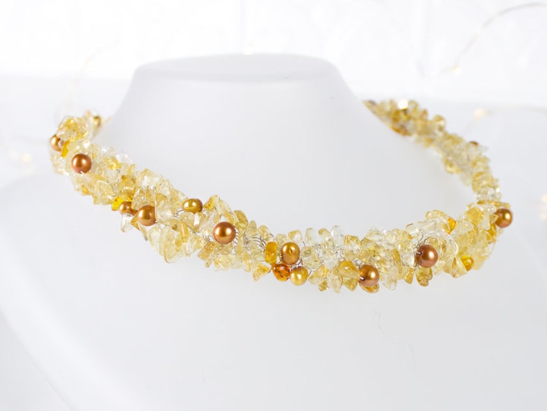 K&ouml;nnte beinhalten: Eine Halskette aus goldenen und gelben Edelsteinen mit kleinen braunen Perlen. Die Kette ist aus Draht gefertigt und zu einer Spirale gedreht.