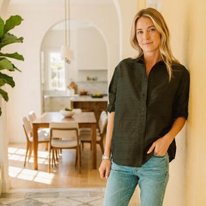 May include: A dark charcoal button-down shirt with a subtle textured finish, paired with light blue denim jeans and black pointed-toe mules. The shirt features a classic collar, long sleeves rolled to the elbows, and a front button closure.