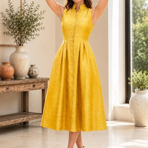 May include: A sleeveless mustard yellow midi dress featuring a mandarin collar, a full button-down front with matching buttons, and a pleated skirt. The fabric has a subtle textured weave, and the dress is fitted at the waist with a flared silhouette.
