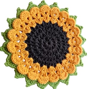 Pode incluir: Um porta-copos redondo de crochê com um centro cinza-carvão escuro, rodeado por um anel de pétalas amarelo-douradas e finalizado com uma borda externa serrilhada de fio verde-claro, criando um padrão de girassol com superfície texturizada.