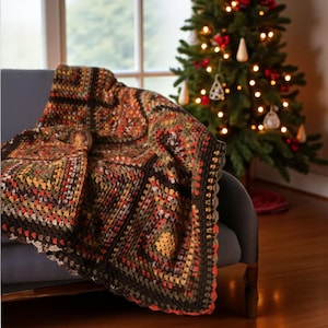 Può includere: Una coperta fatta a mano, all'uncinetto con un motivo a quadrati granny. La coperta presenta un mix di colori caldi, tra cui marrone, arancione, verde e giallo. La coperta è drappeggiata su una poltrona grigia, con un albero di Natale sullo sfondo.