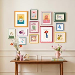 May include: A gallery wall arrangement featuring twelve colorful framed prints with scalloped edges, displaying various illustrations including a cake, matcha latte, and Paris text. Below, a wooden console table holds three dog-shaped ceramic vases.