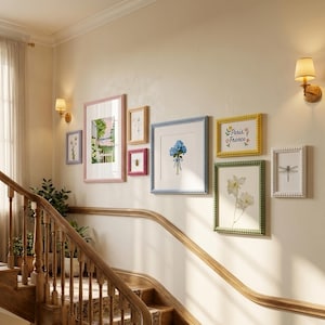 May include: A collection of framed art pieces with various floral and nature-themed prints, arranged on a beige wall. Frames are in shades of pink, blue, yellow, and white, with beaded edges. The text "Paris, France" is visible on one frame.