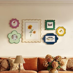 Könnte beinhalten: Eine Galerie-Wandgestaltung mit sechs dekorativen Rahmen mit gewellten Rändern in verschiedenen Farben wie Pink, Hellgrün, Creme, Dunkelgrün, Gelb und Dunkelblau, die botanische Illustrationen, Schmetterlinge und Fische zeigen.