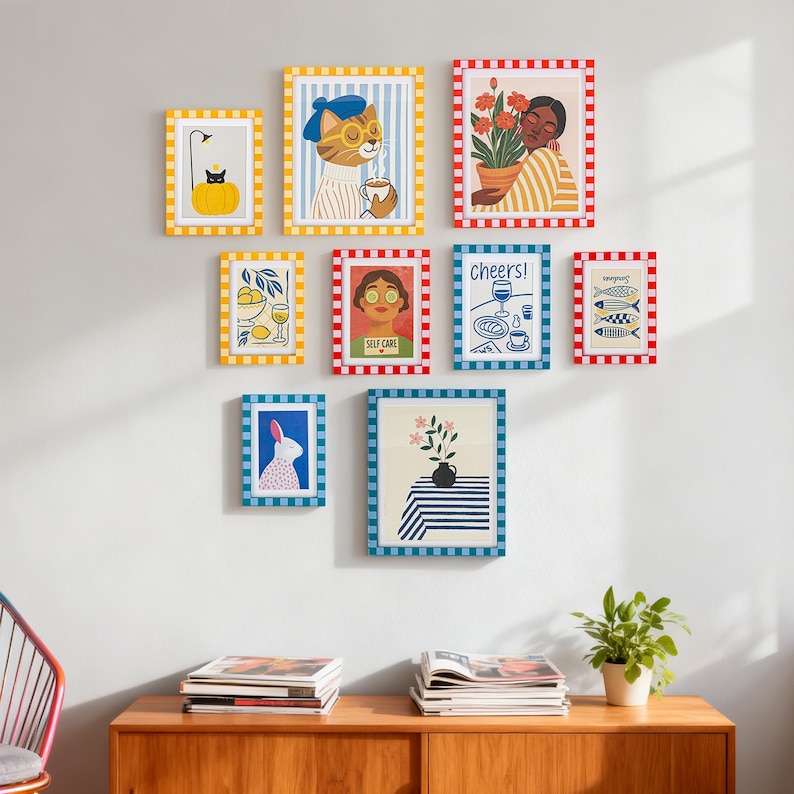 May include: A collection of framed art prints with various illustrations. The prints feature a cat with a beret, a person with flowers, a rabbit, lemons, fish, and the words "Cheers!" and "Self Care." The frames have colorful striped and checkered patterns.