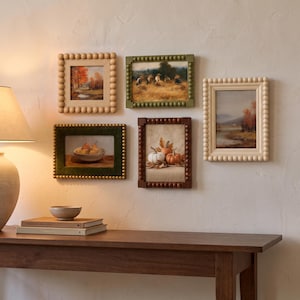 May include: A gallery wall arrangement featuring five rectangular picture frames with beaded edges. The frames are in various colors including light wood, olive green, dark brown, and cream, displaying landscape and still life art prints.