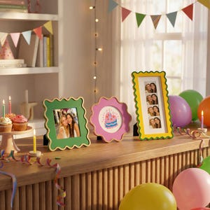 May include: Three wavy-edged picture frames in green, pink, and yellow. The square green frame holds a photo of two people, the round pink frame displays a birthday cake illustration, and the tall yellow frame contains a vertical photo strip.