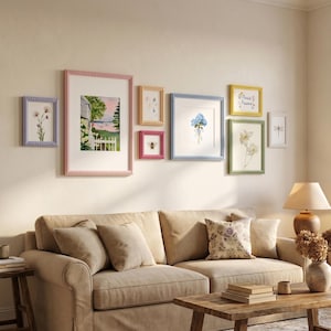 May include: A collection of framed art pieces in various sizes and colors, including pink, blue, yellow, and green. The artwork features floral and landscape themes, creating a cohesive gallery wall arrangement. The frames have beaded edges.