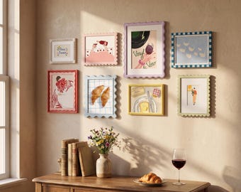 May include: A gallery wall featuring eight framed art prints with scalloped edges in various colours, including illustrations of Paris, croissants, and wine. The prints are arranged on a beige wall above a wooden console table with books.