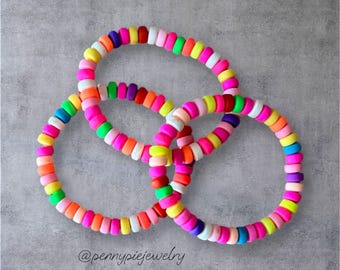 May include: Three colorful beaded bracelets with a variety of bright colors, including pink, yellow, green, blue, and purple. The bracelets are stacked on top of each other, creating a layered effect. The text '@pennypiejewelry' is visible at the bottom of the image.