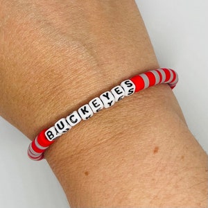 May include: A red and white beaded bracelet with the word "BUCKEYES" spelled out in black letters on white beads.